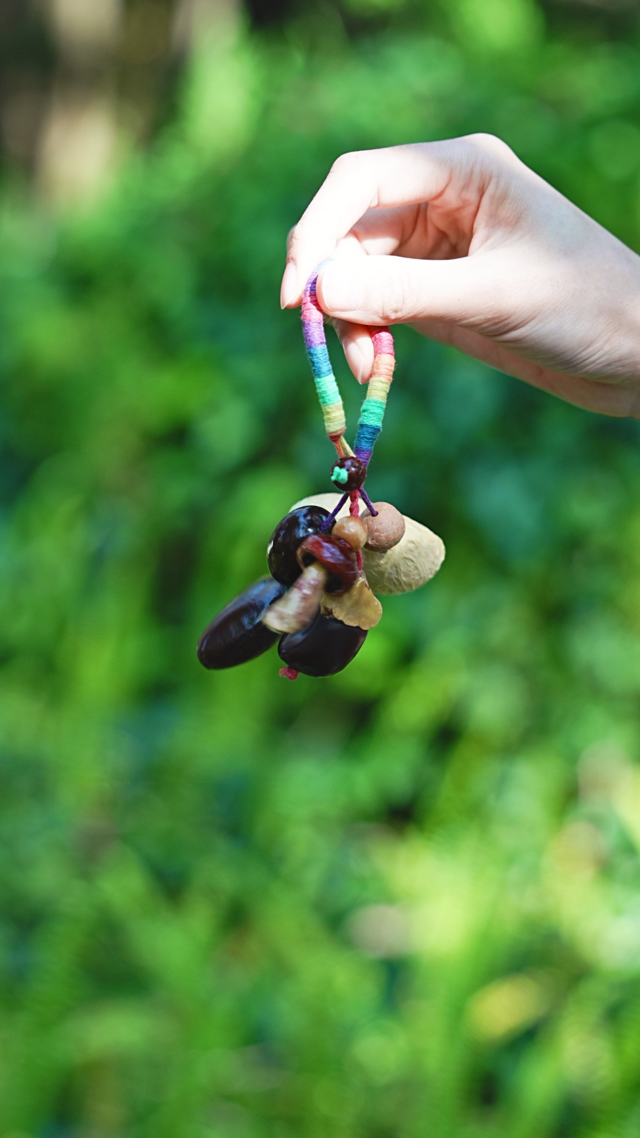Rainbow Forager mushroom seed charm with bright wrap and dark seed pods held outdoors