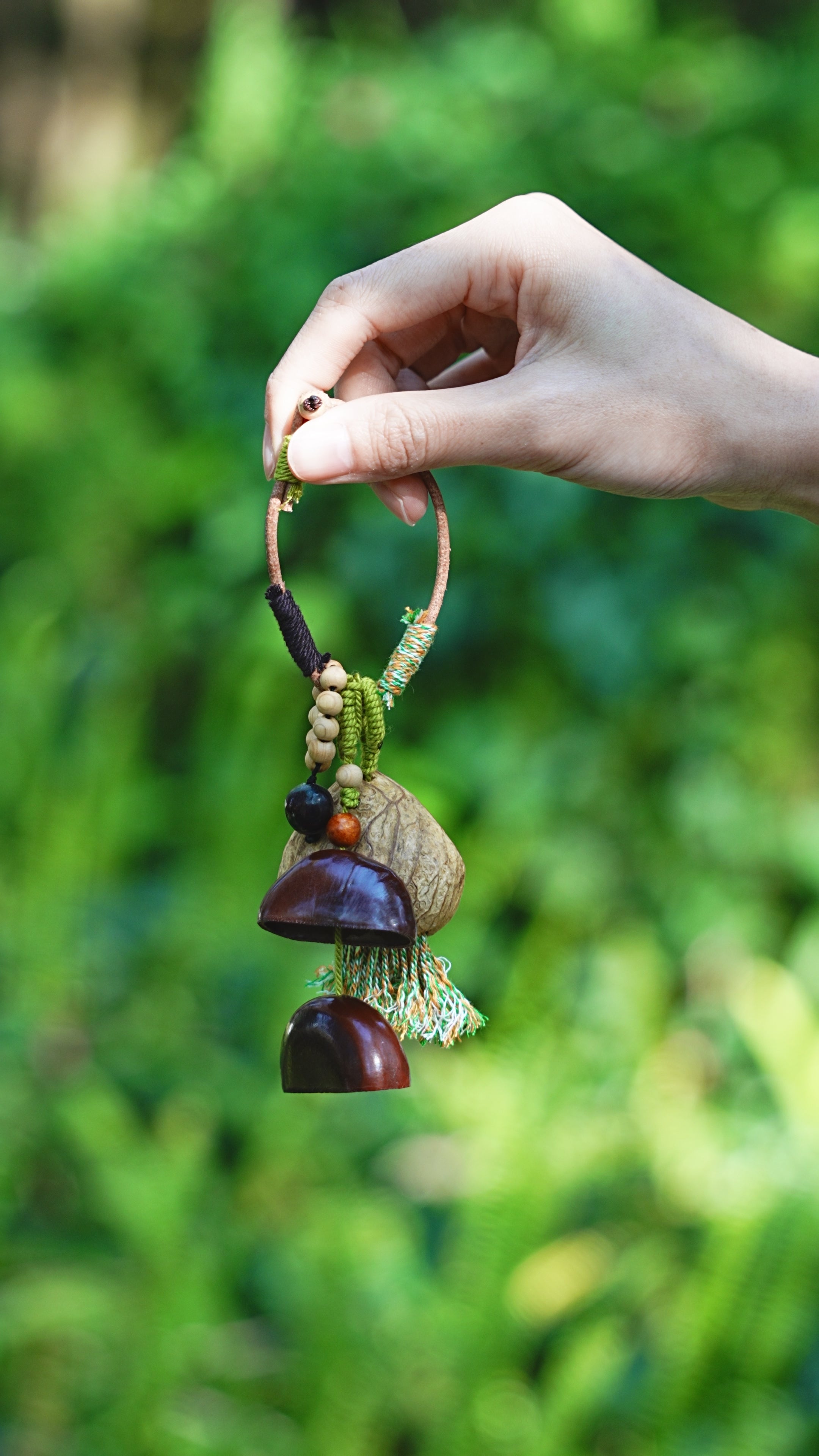 Forest Bell seed tassel charm with green cord and dark seed bells held outdoors