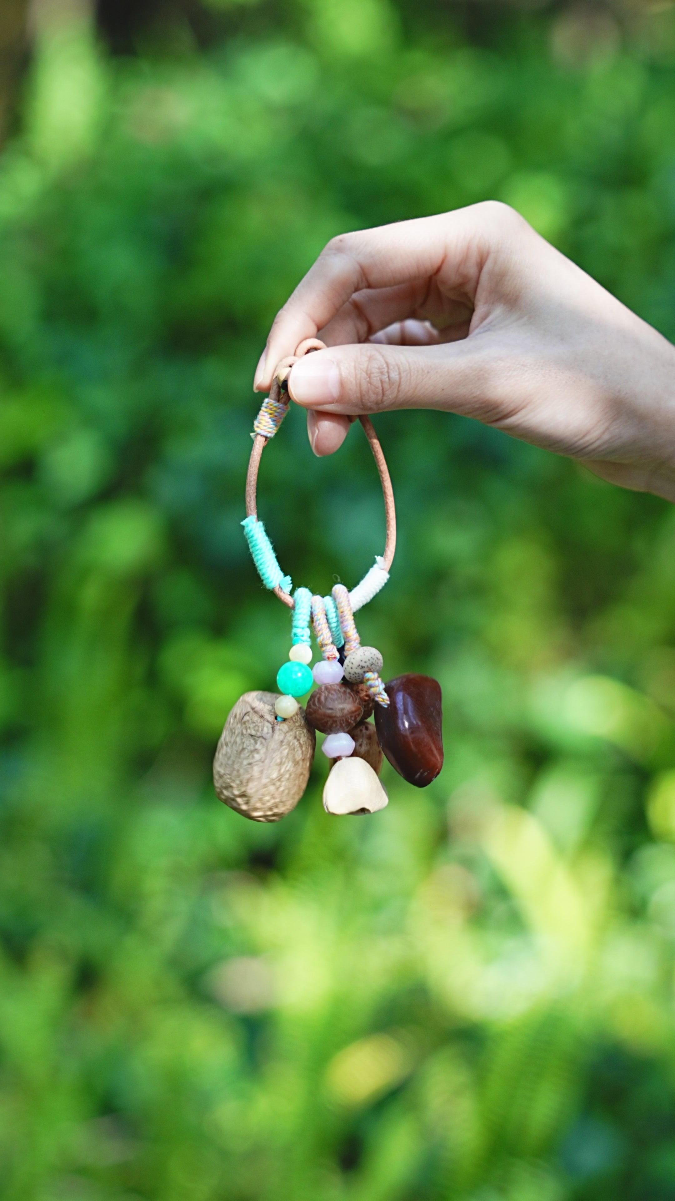 Mint green wrapped seed charm with turquoise beads and shell tassels held outdoors