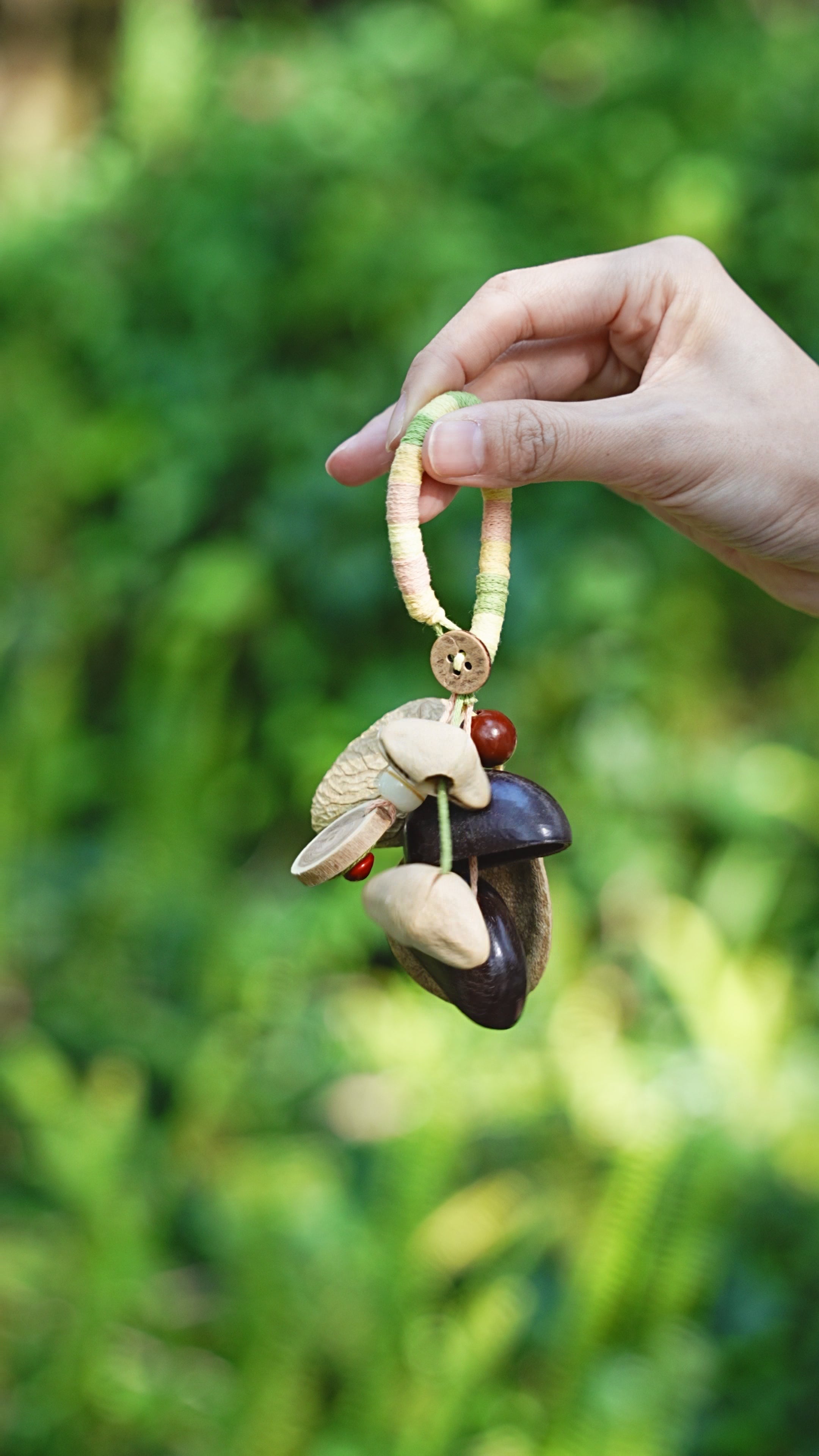 Pastel Picnic olive seed charm with cream cord and dark seed pods held outdoors